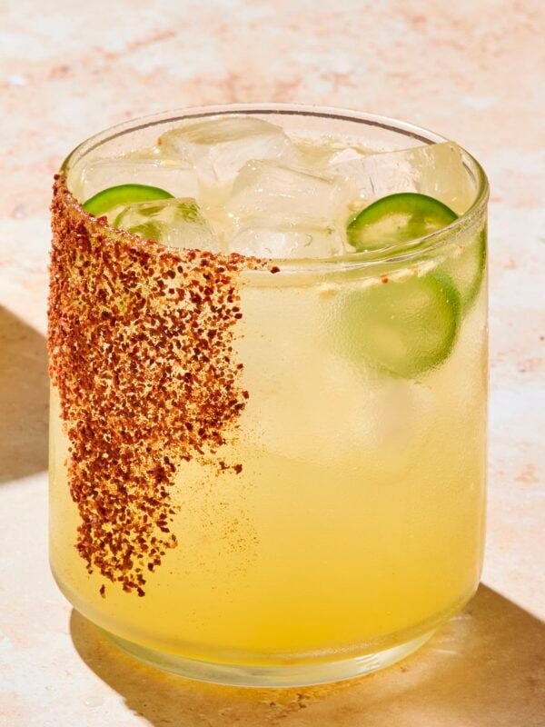 Glass with tajin on rim filled with spicy margarita with jalapenos in glass.