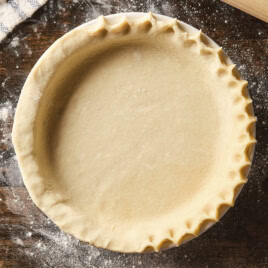 Pie crust in a baking dish with edges being crimped before being baked.