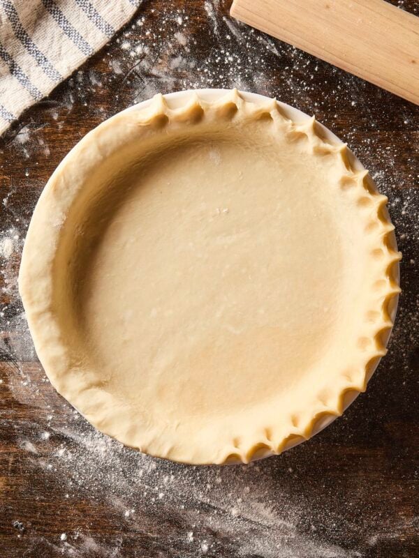 Pie crust in a baking dish with edges being crimped before being baked.