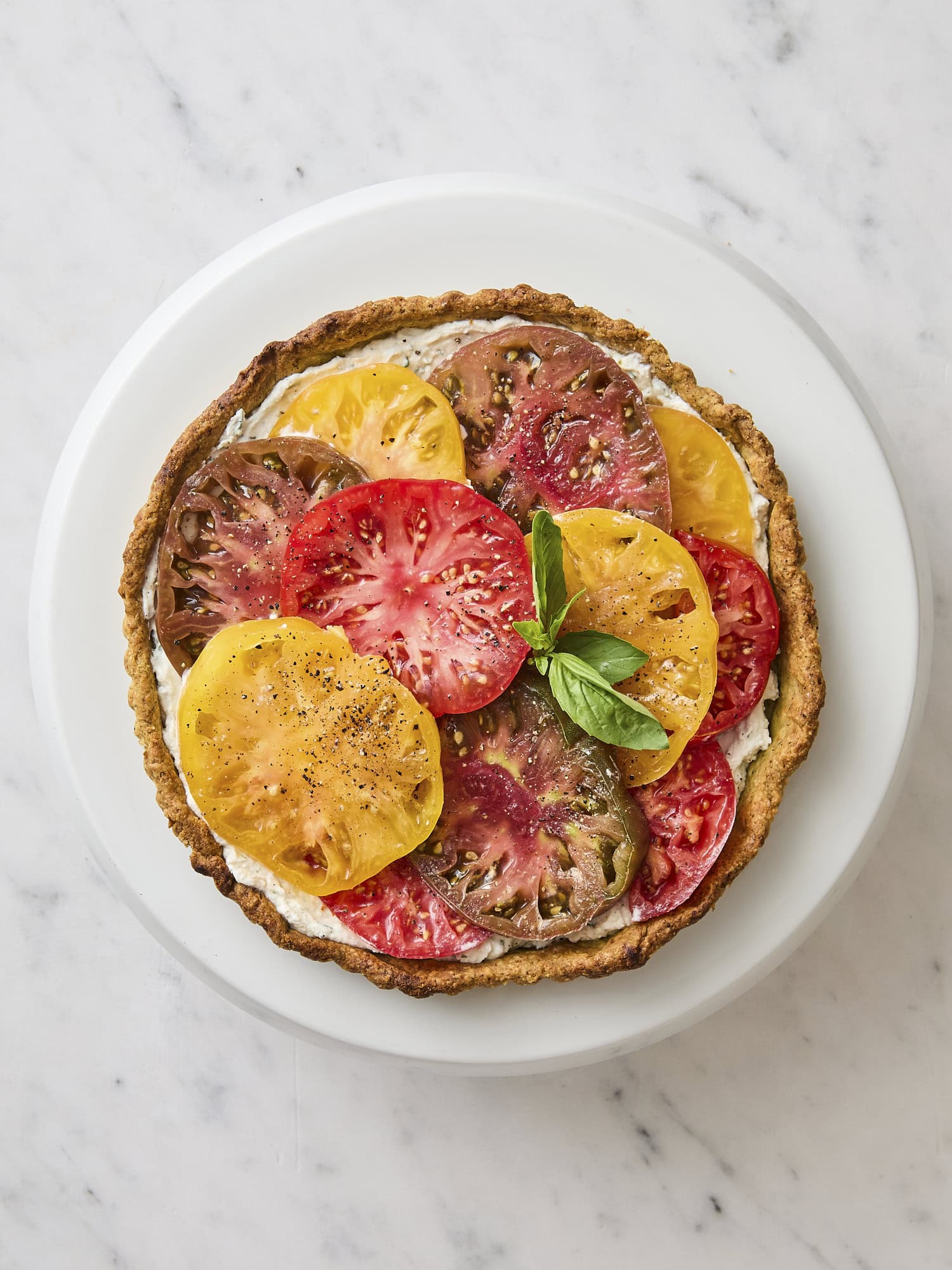 White marble surface with plate with tomato tart on top.