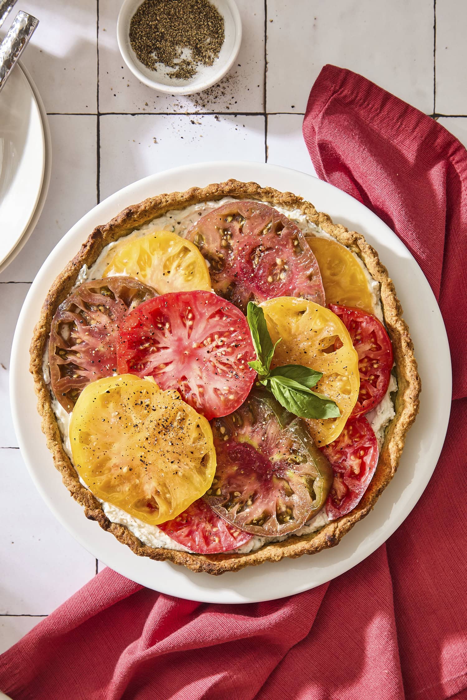 Round plate with baked tomato tart with brightly colored slices of fresh tomato on top.