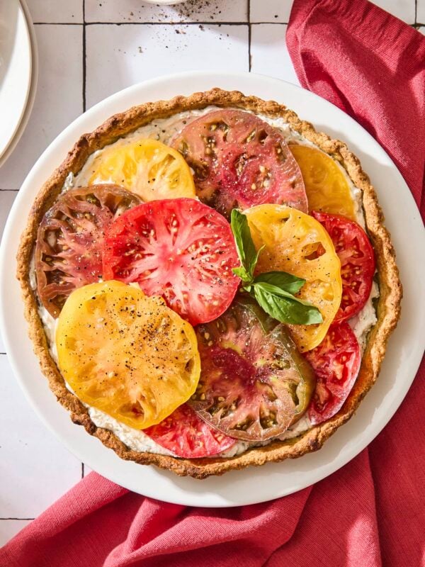 Tile surface with baked tomato tart with slices of tomato shingled on top garnished with fresh basil.