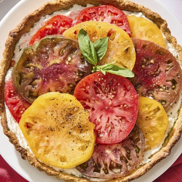 White plate with baked tomato tart on top with fresh basil garnish.