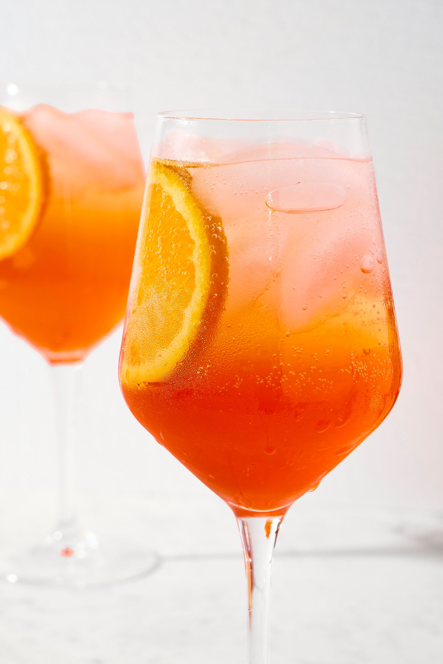Ombre colored Aperol spritz cocktail in a wine glass with an orange slice.