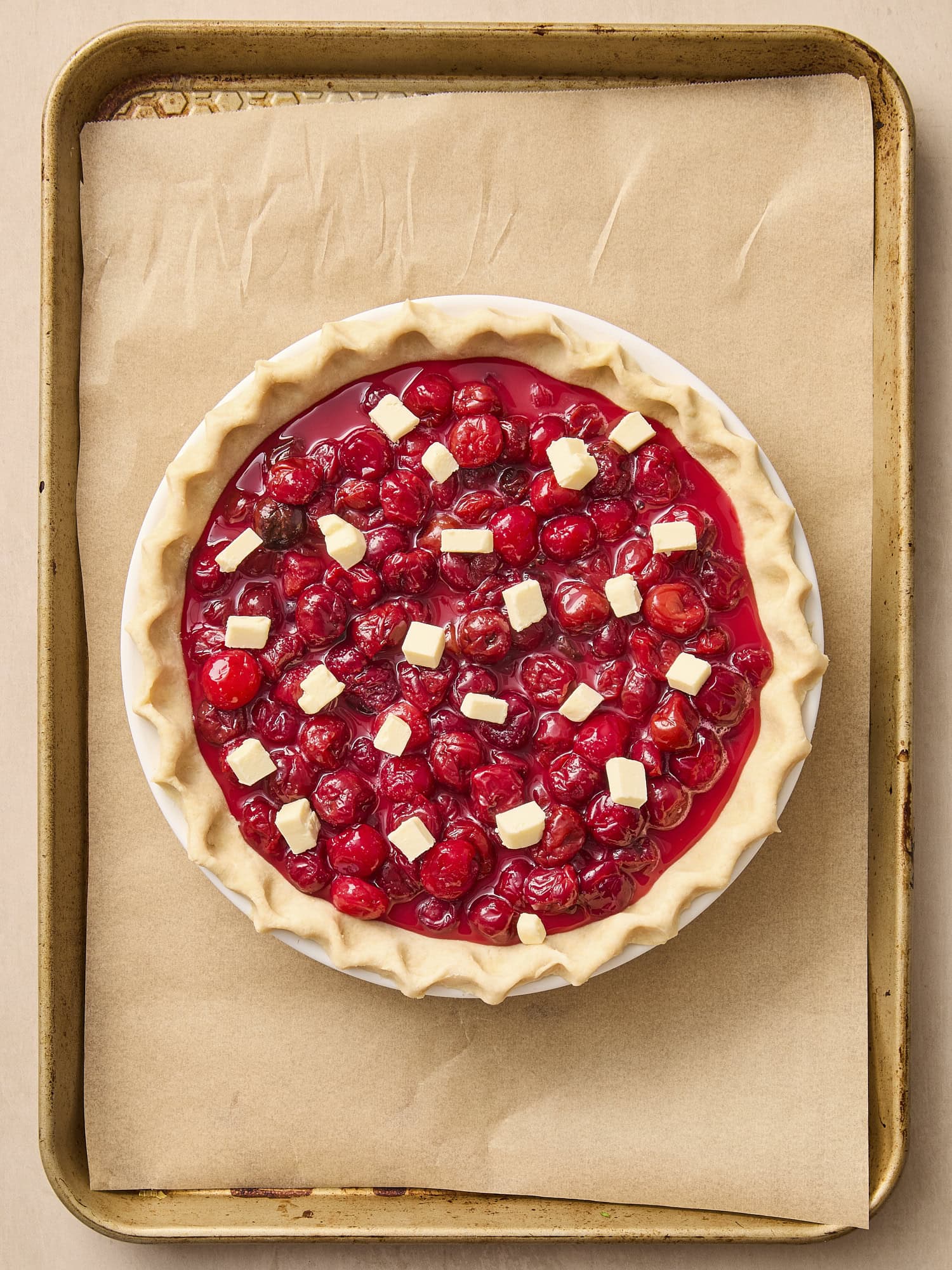Unbaked cherry pie with pieces of butter on a baking sheet.