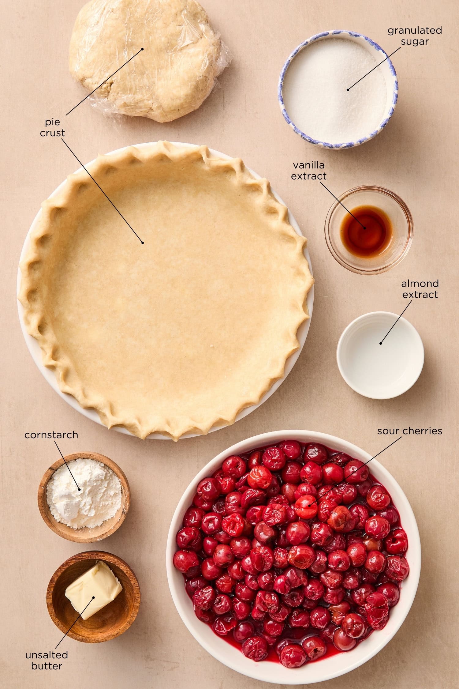 Surface with ingredients for a cherry pie including cherries, sugar, pie crust, and more.
