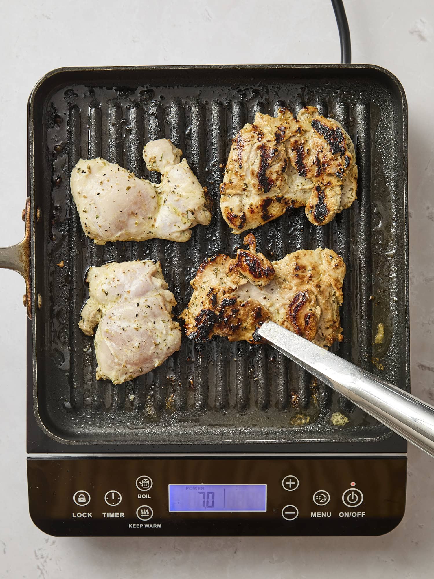 Chicken thighs grilling on a grill pan with charred edges.