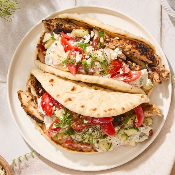 White plate with two chicken gyros with Greek salad topping and feta cheese.