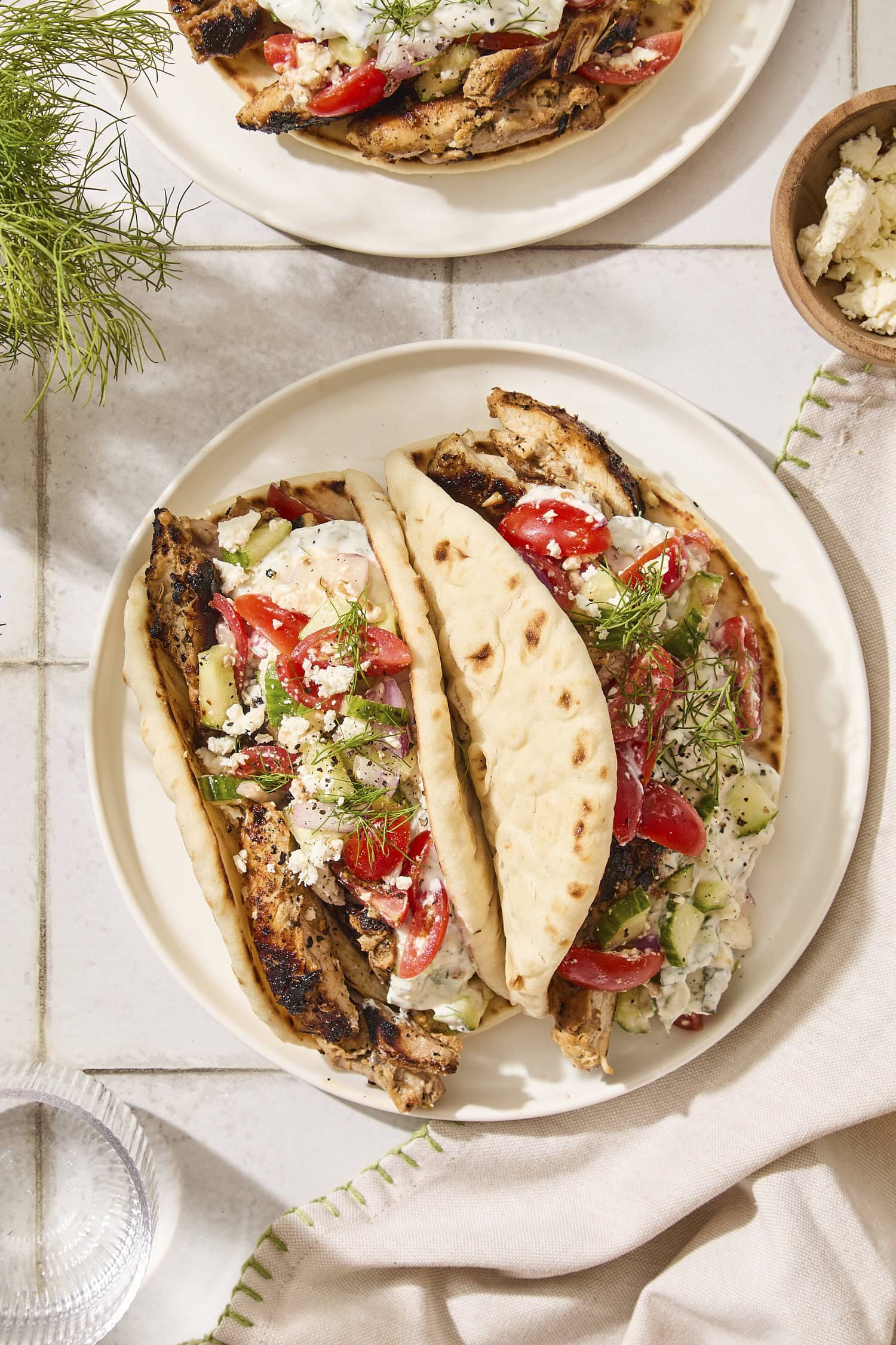 Plate with two chicken gyros topped with tomato and cucumber salad and tzatziki sauce.