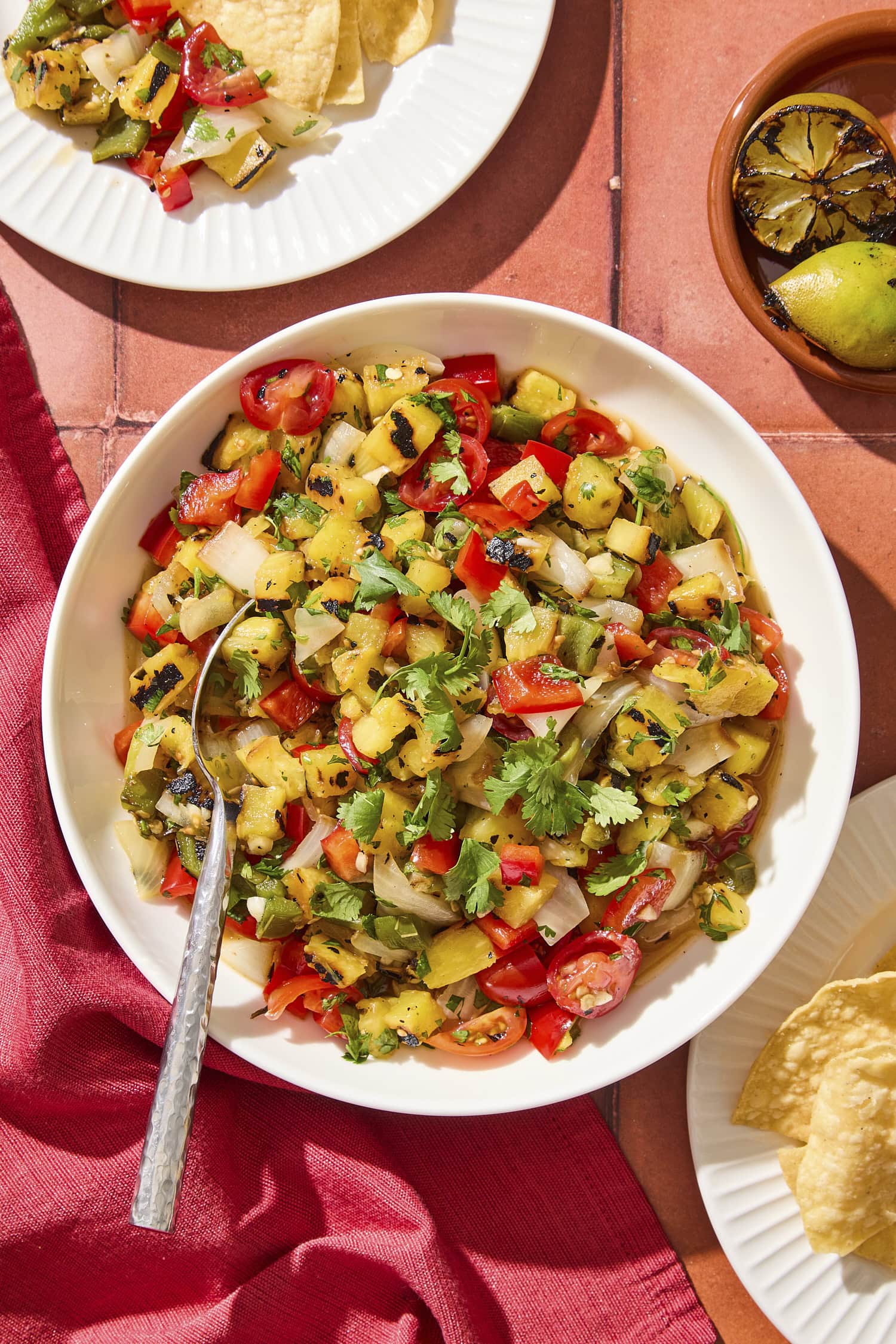 Tile surface with bowl of grilled pineapple salsa with chips to the side.