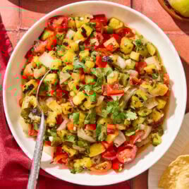 White bowl filled with chunky pineapple salsa with tomatoes and herbs.