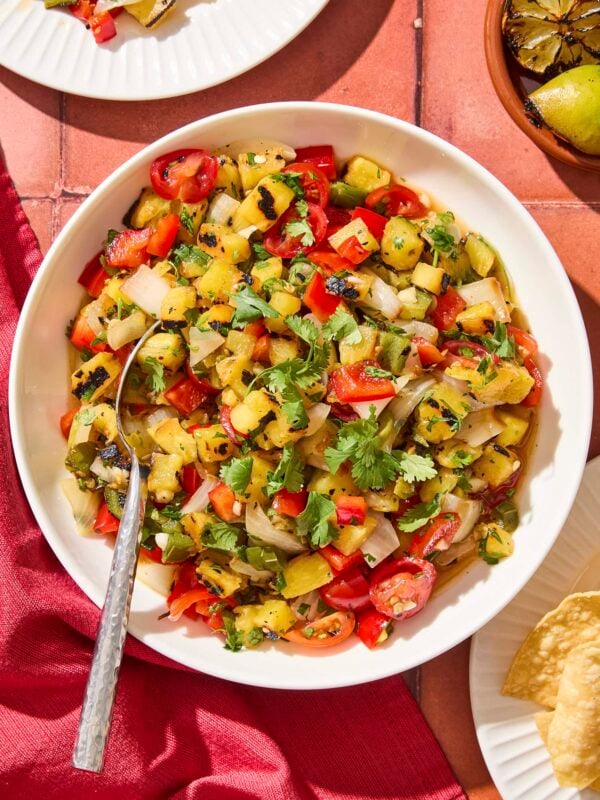 White bowl filled with chunky pineapple salsa with tomatoes and herbs.