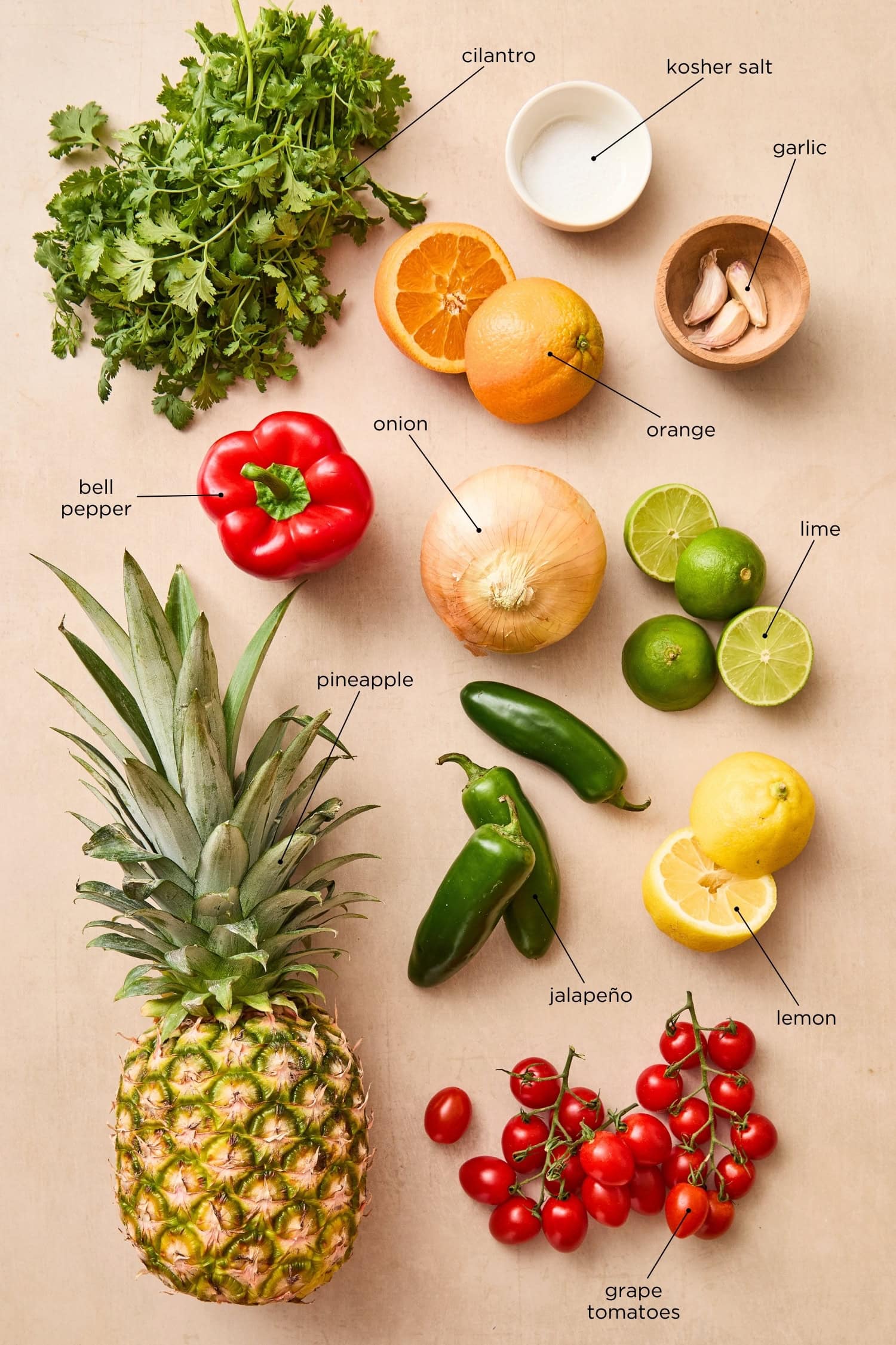 Ingredients needed for grilled pineapple salsa including citrus, herbs, tomatoes, and pineapple.