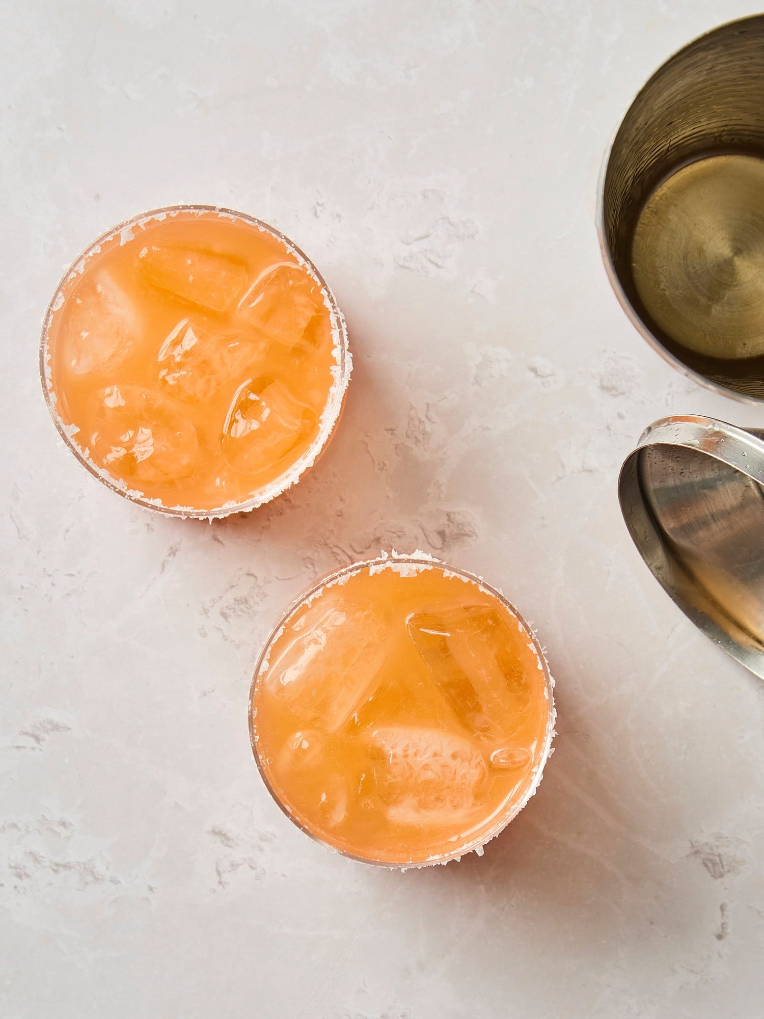 Gray surface with two Italian margarita drinks with shaker to the side.