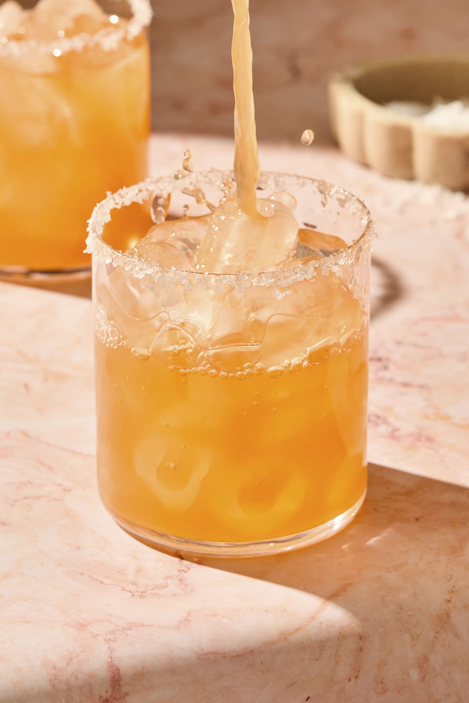 Orange colored margarita splashing into a glass filled with ice.