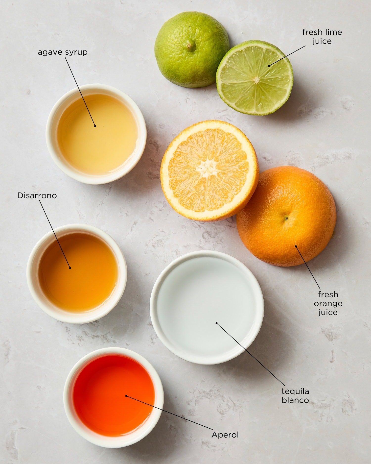Surface with ingredients to make an Italian margarita including alcohol, agave, and citrus.