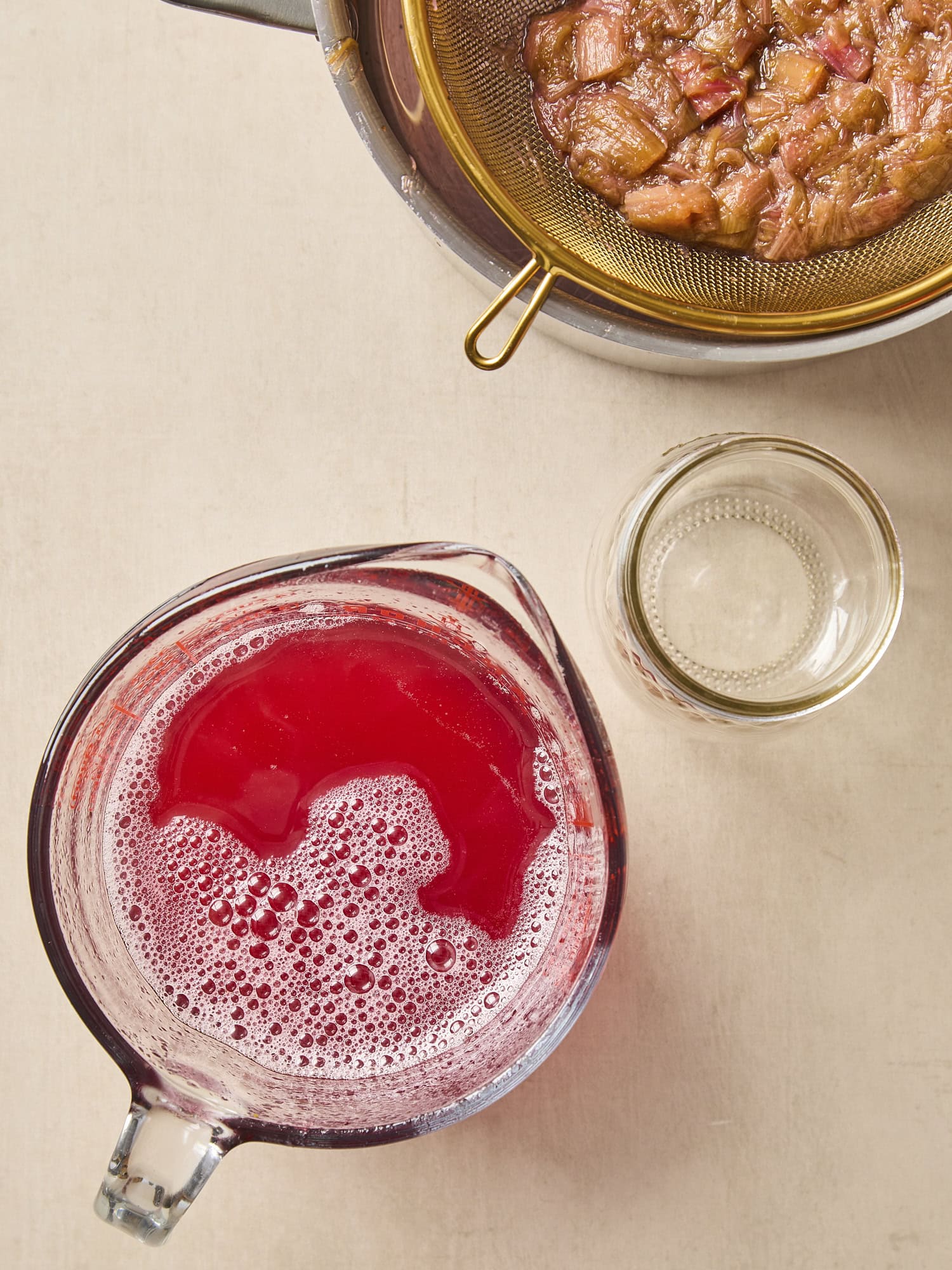 Surface with rhubarb simple syrup with leftover cooked rhubarb to the side.