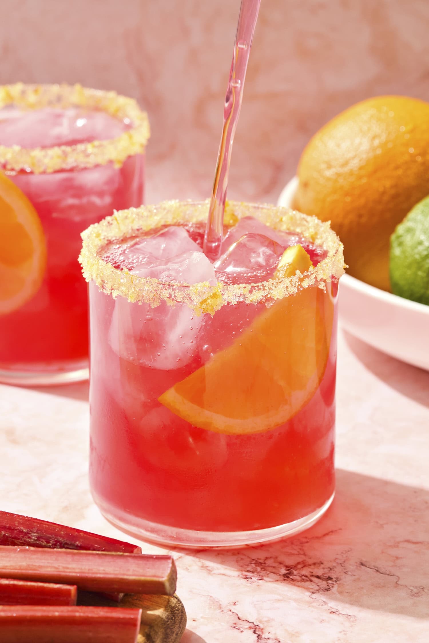 Rhubarb margarita being poured into a glass with orange salt rim.