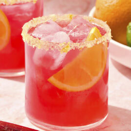 Rhubarb margarita with orange salt rim with wedge of orange.