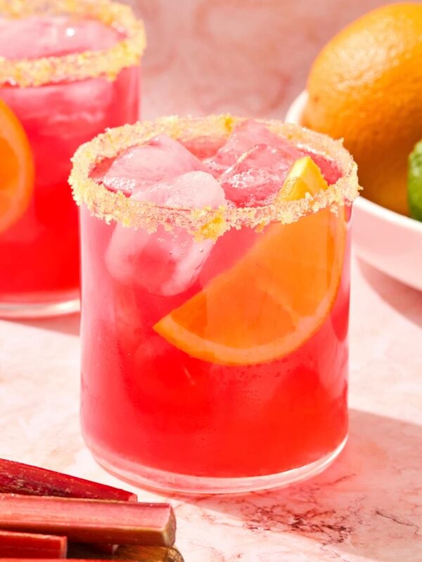 Rhubarb margarita with orange salt rim with wedge of orange.