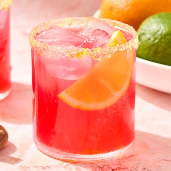 Glass filled with pink colored margarita with orange slice.
