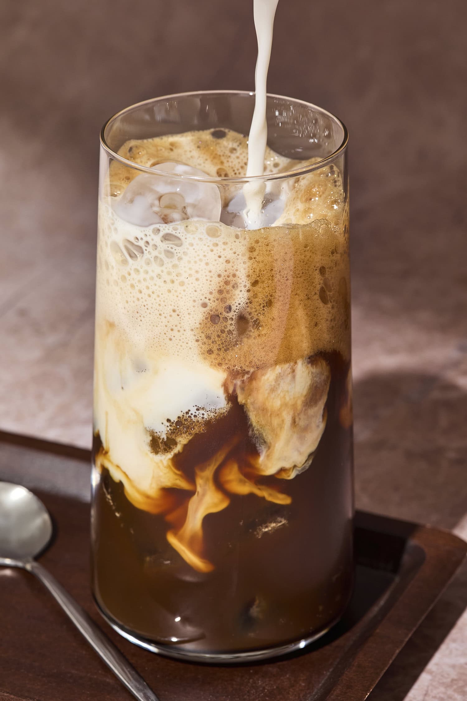 Glass with milk pouring on top of a shaken espresso.