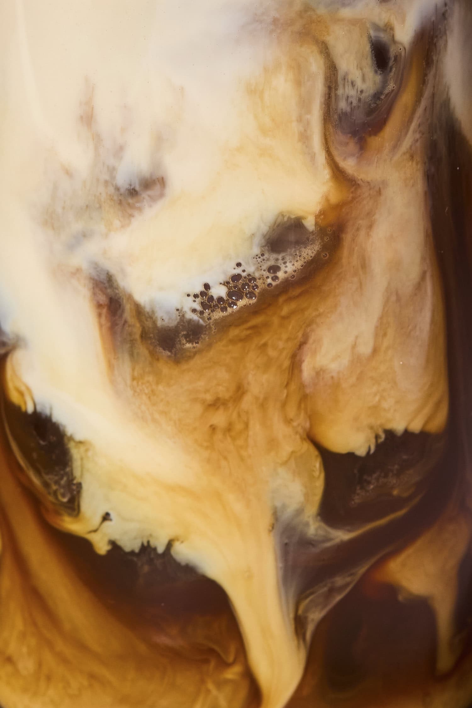 Milk mixing with coffee in a tall glass.