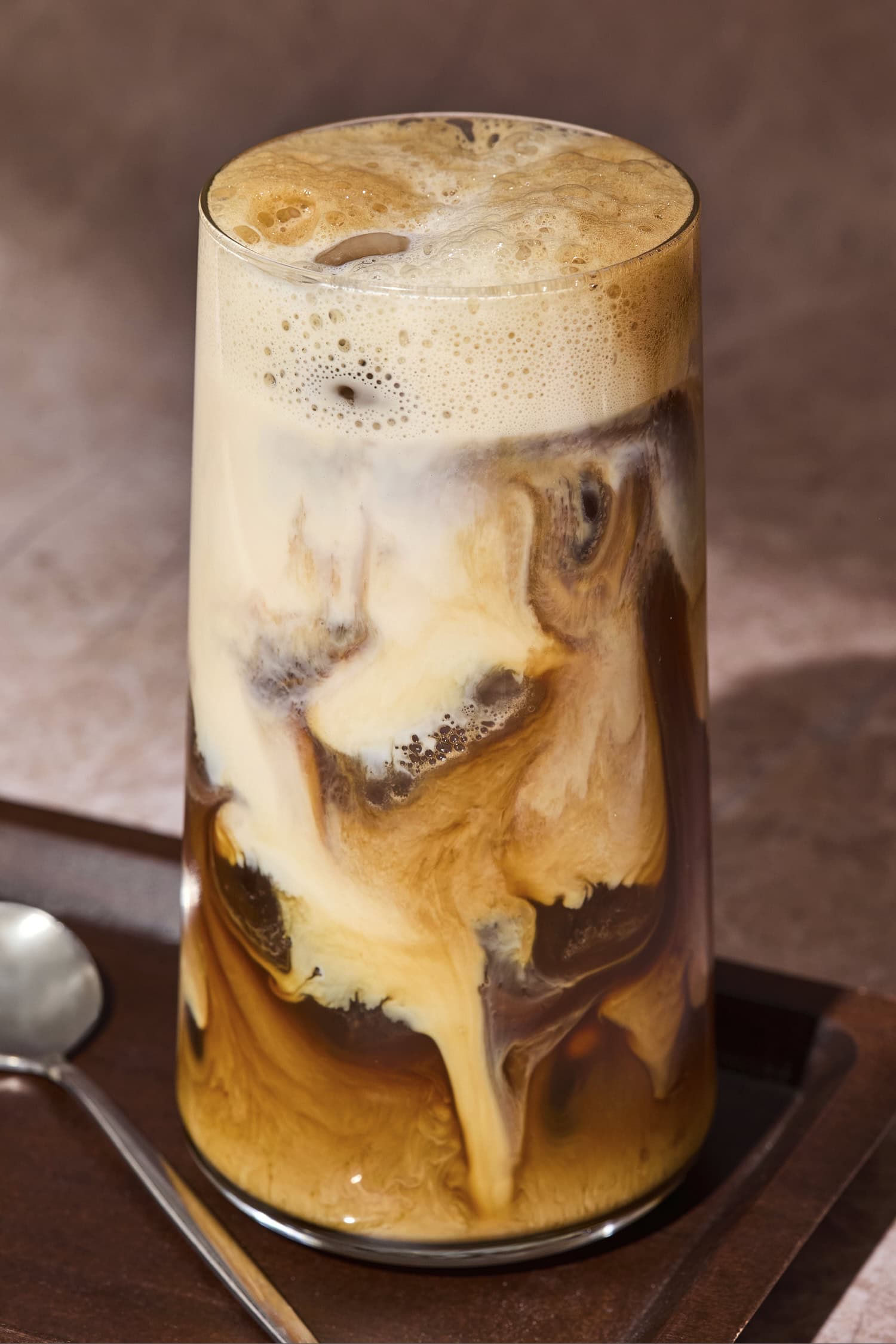 Tall glass with shaken espresso with milk mixture pouring throughout.