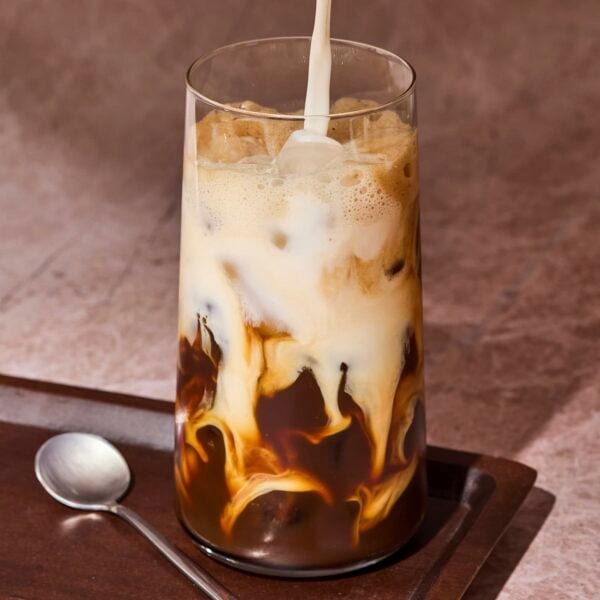 Milk pouring into a tall glass with shaken espresso and ice.