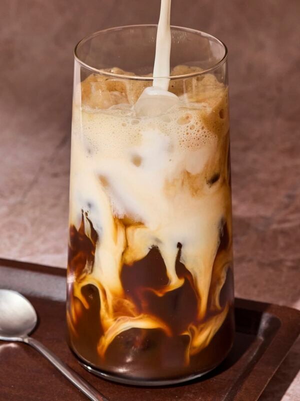 Milk pouring into a tall glass with shaken espresso and ice.