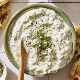 Bowl filled with creamy white tzatziki sauce with spoon.