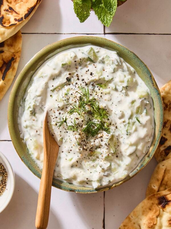 Bowl filled with creamy white tzatziki sauce with spoon.
