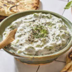 Bowl filled with tzatziki sauce with dill on top.