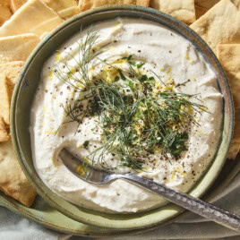 Green bowl filled with whipped feta dip topped with herbs and lemon zest.