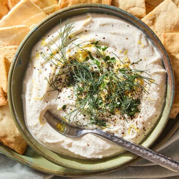 Green bowl filled with whipped feta dip topped with herbs and lemon zest.