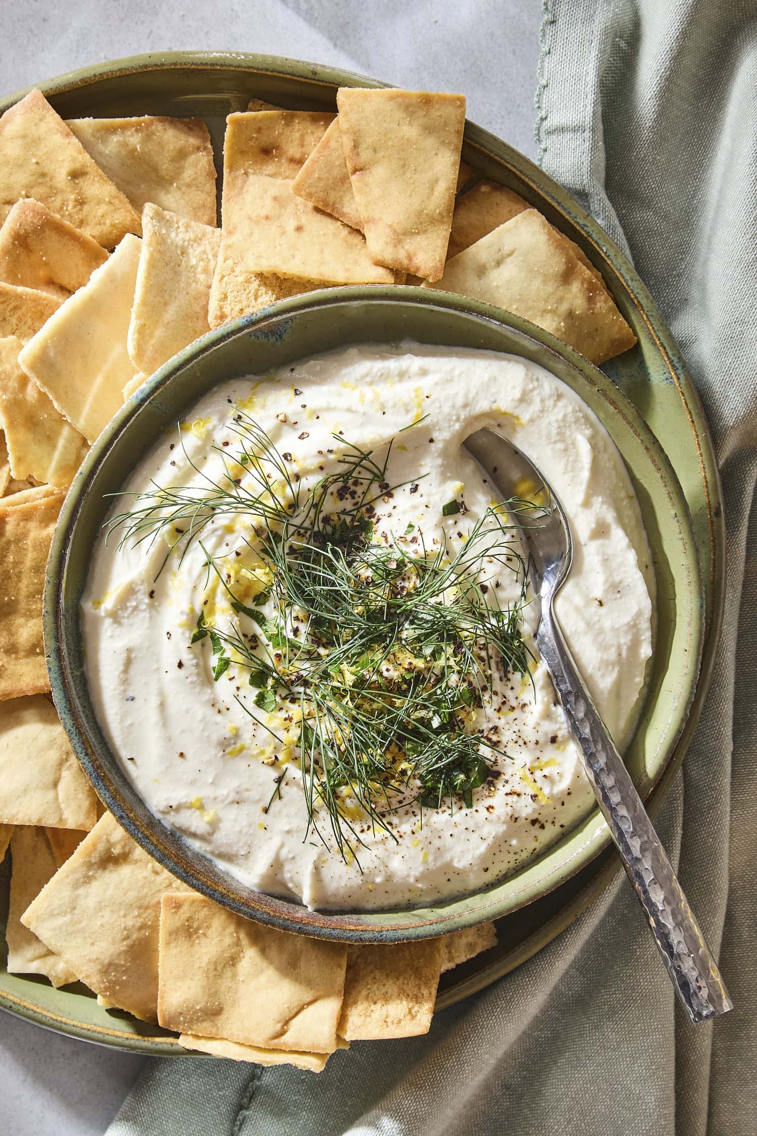 Plate with pita chips and feta dip topped with herbs and lemon zest.