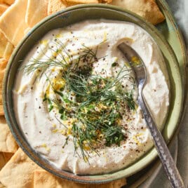 Whipped feta dip spread into a bowl topped with herbs and lemon zest with pita chips around.