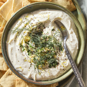 Whipped feta dip spread into a bowl topped with herbs and lemon zest with pita chips around.