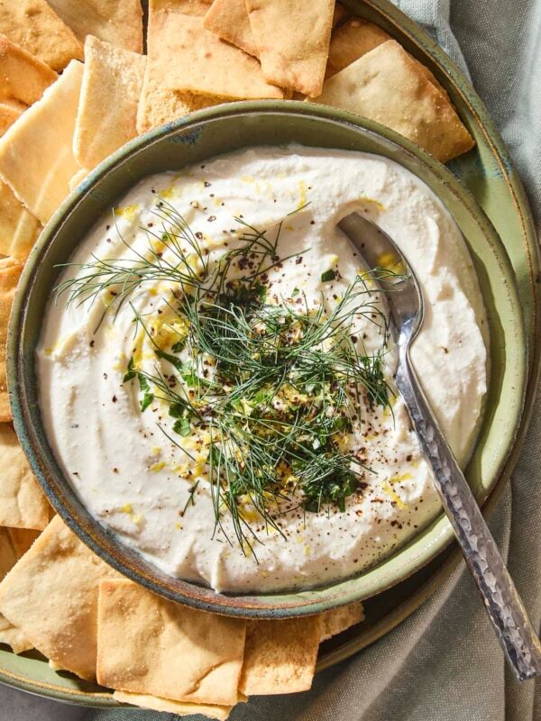Whipped feta dip spread into a bowl topped with herbs and lemon zest with pita chips around.
