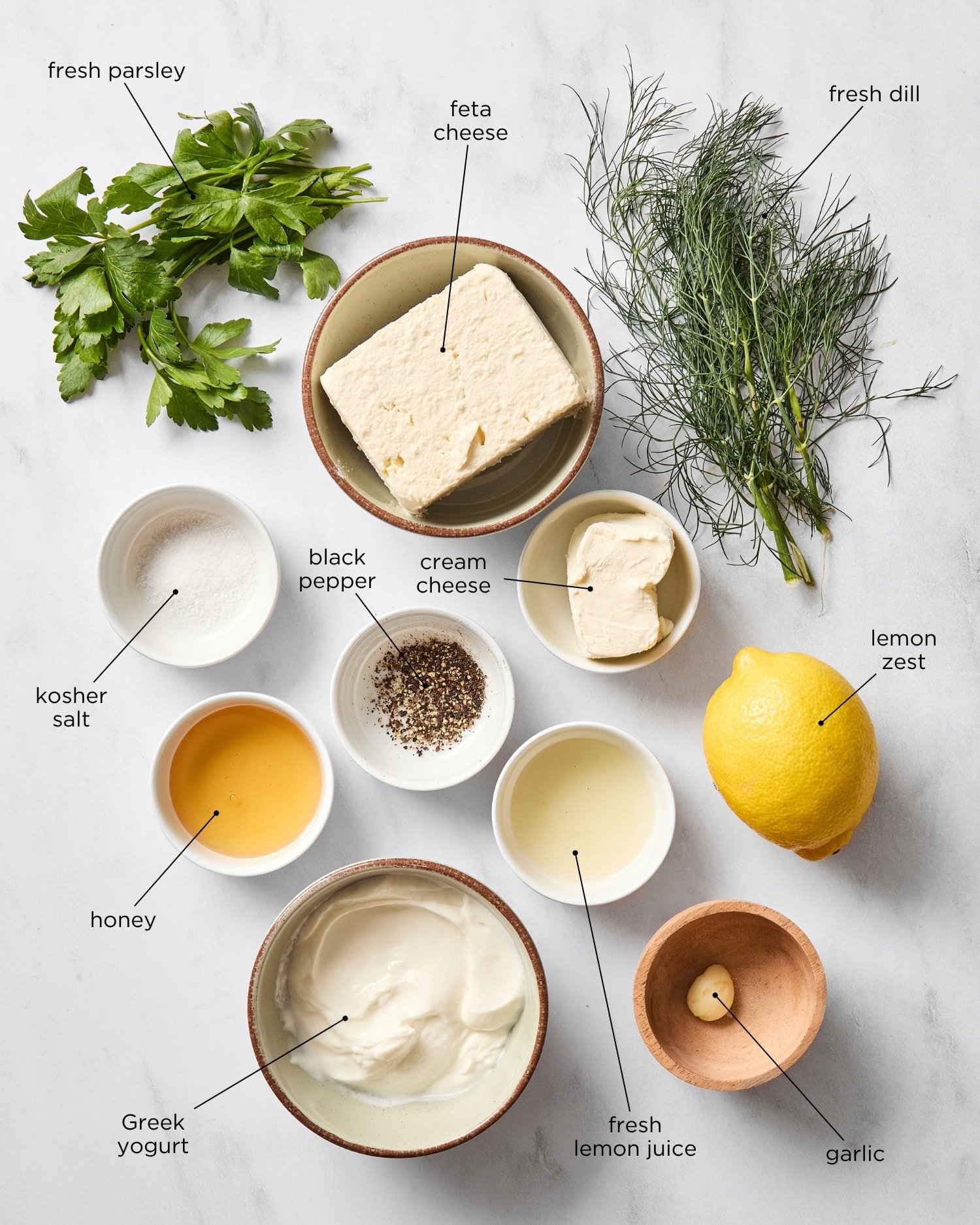 Marble surface filled with ingredients for a whipped feta dip including feta, lemon, yogurt, spices, herbs, and more.