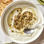 Bowl with whipped goat cheese with pistachios and honey on top with spoon scooping up serving.