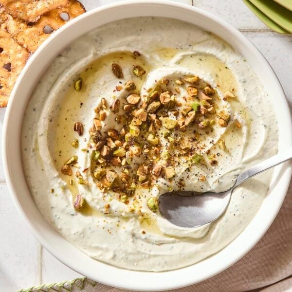 Bowl with whipped goat cheese with pistachios and honey on top with spoon scooping up serving.