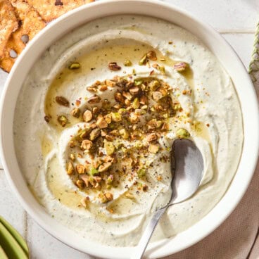 White bowl filled with whipped goat cheese topped with pistachios and hot honey.