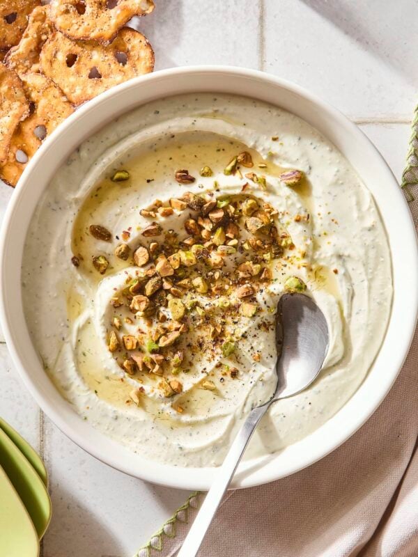 White bowl filled with whipped goat cheese topped with pistachios and hot honey.