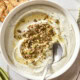 White bowl filled with whipped goat cheese topped with pistachios and hot honey.