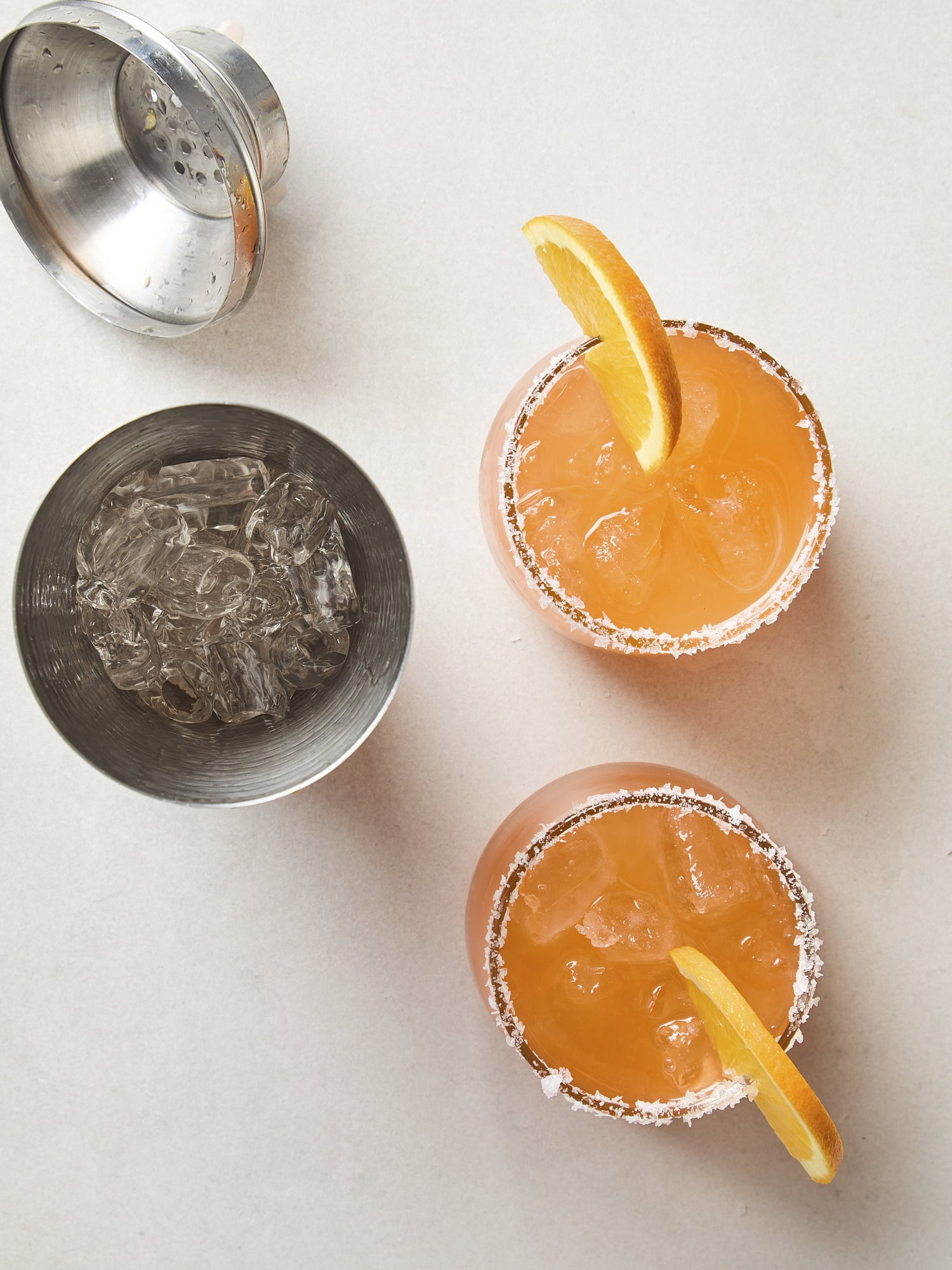 White surface with two Aperol margaritas from a cocktail shaker.