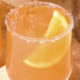 Coral-colored margarita sitting on a stone surface with an orange wedge in the drink.