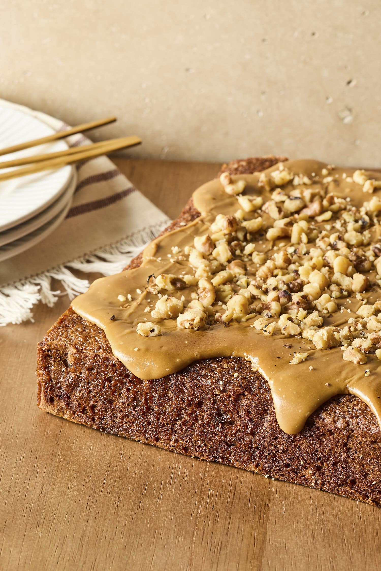 Cake on a wooden board with caramel frosting and walnuts on top.