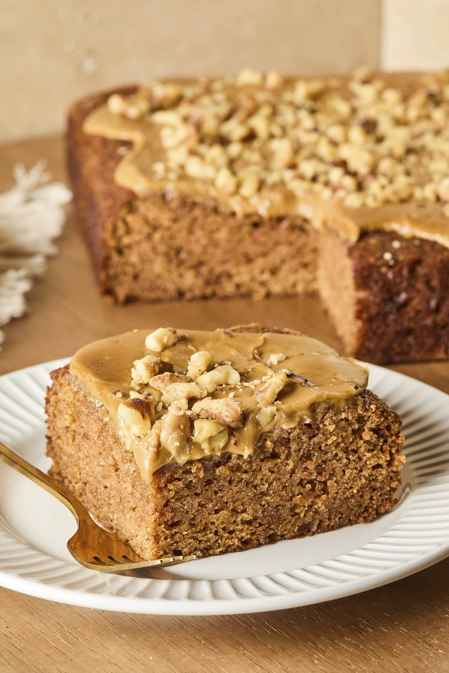 Square piece of applesauce cake with caramel frosting sitting on a white plate.