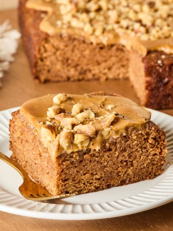 Slice of applesauce cake sitting on a white plate with rest of the cake in the background.